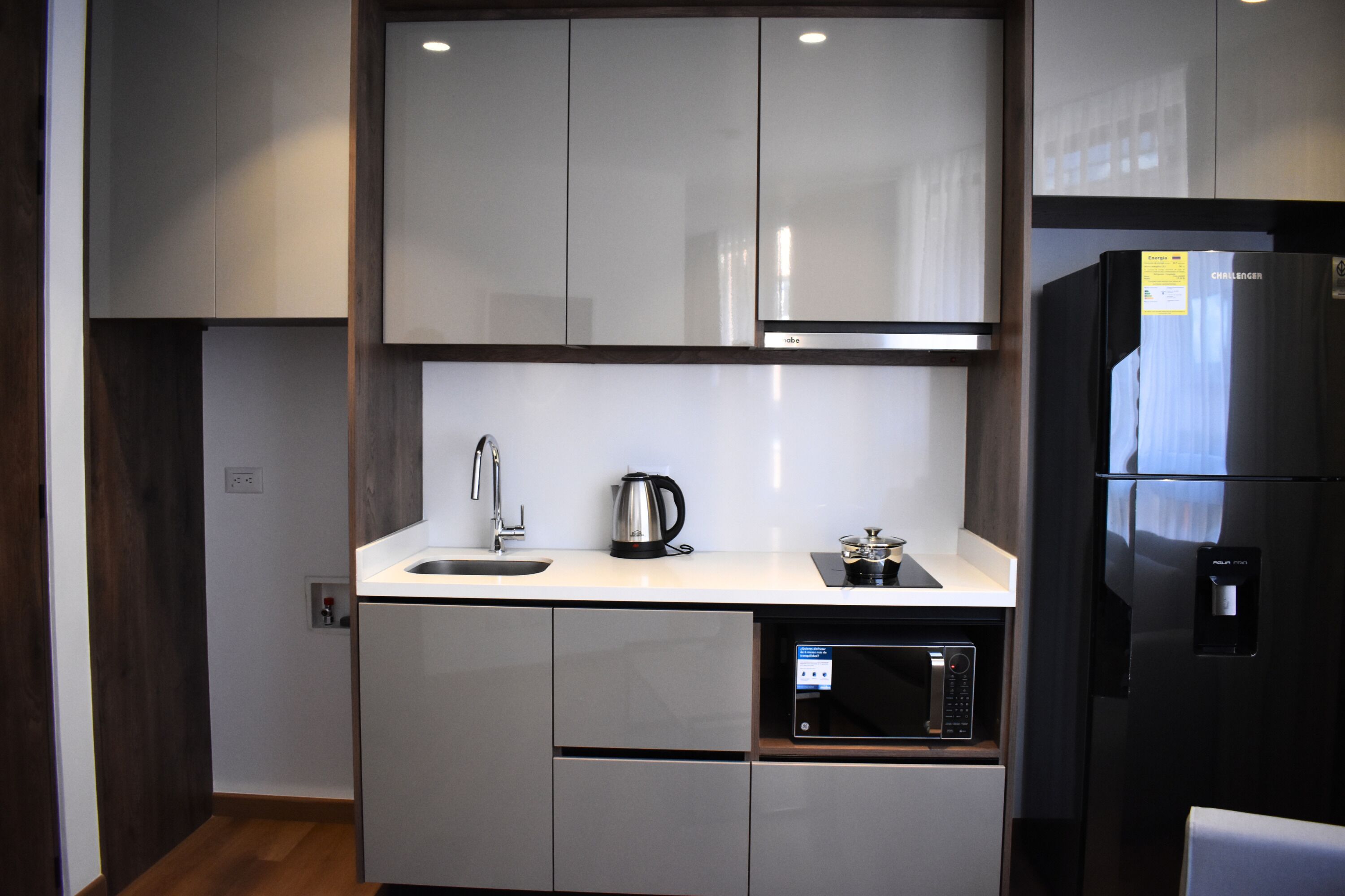 Una cocina moderna con armarios blancos, un microondas integrado y un hervidor de acero inoxidable.