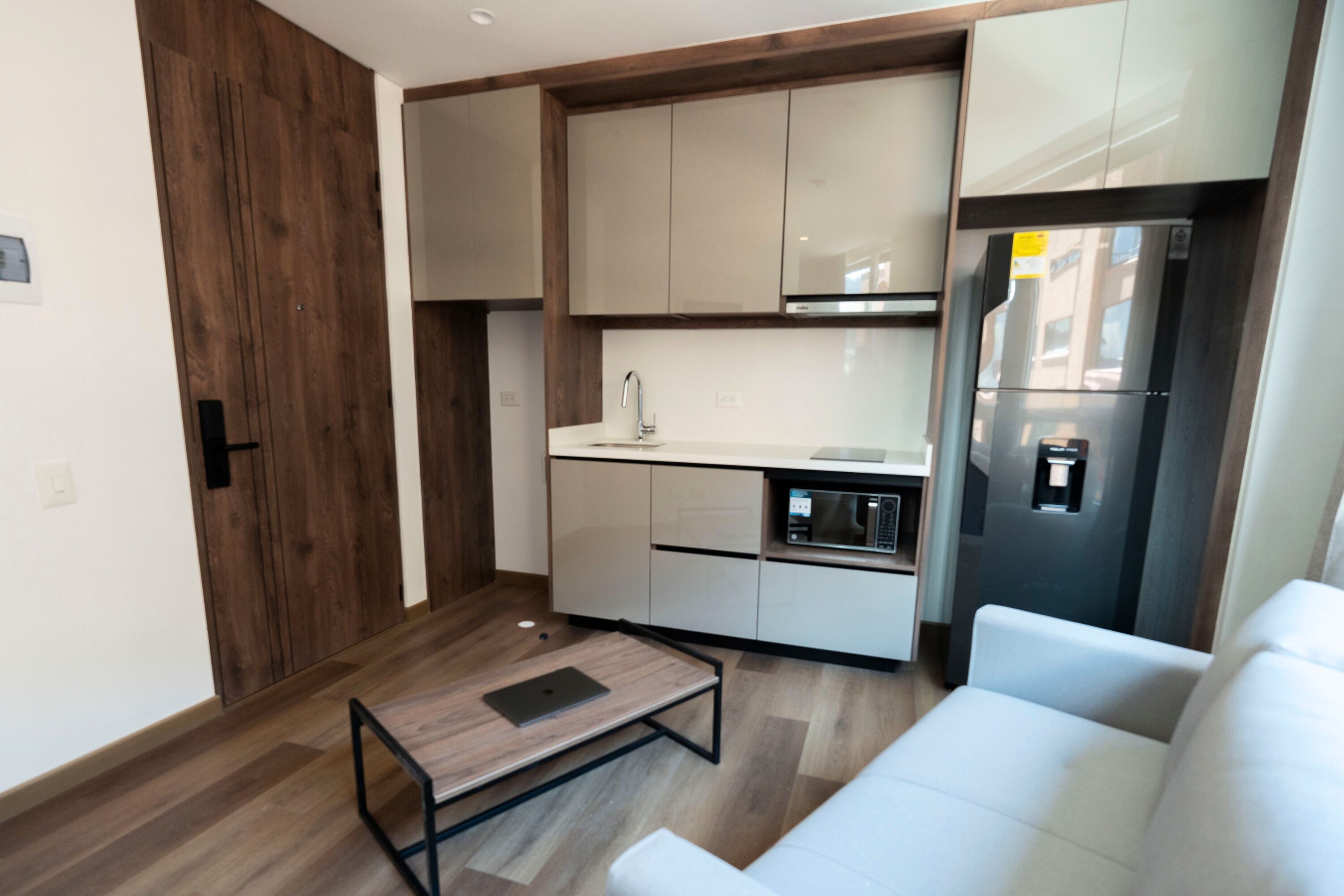 A modern kitchen with white cabinets, a stainless steel refrigerator, and a wooden floor.