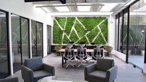 Une salle de réunion moderne avec un mur vert, des chaises grises et une table en verre.