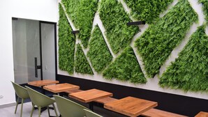 Une salle de conférence avec des tables et des chaises en bois, une porte en verre et un mur décoré de feuillages verts.