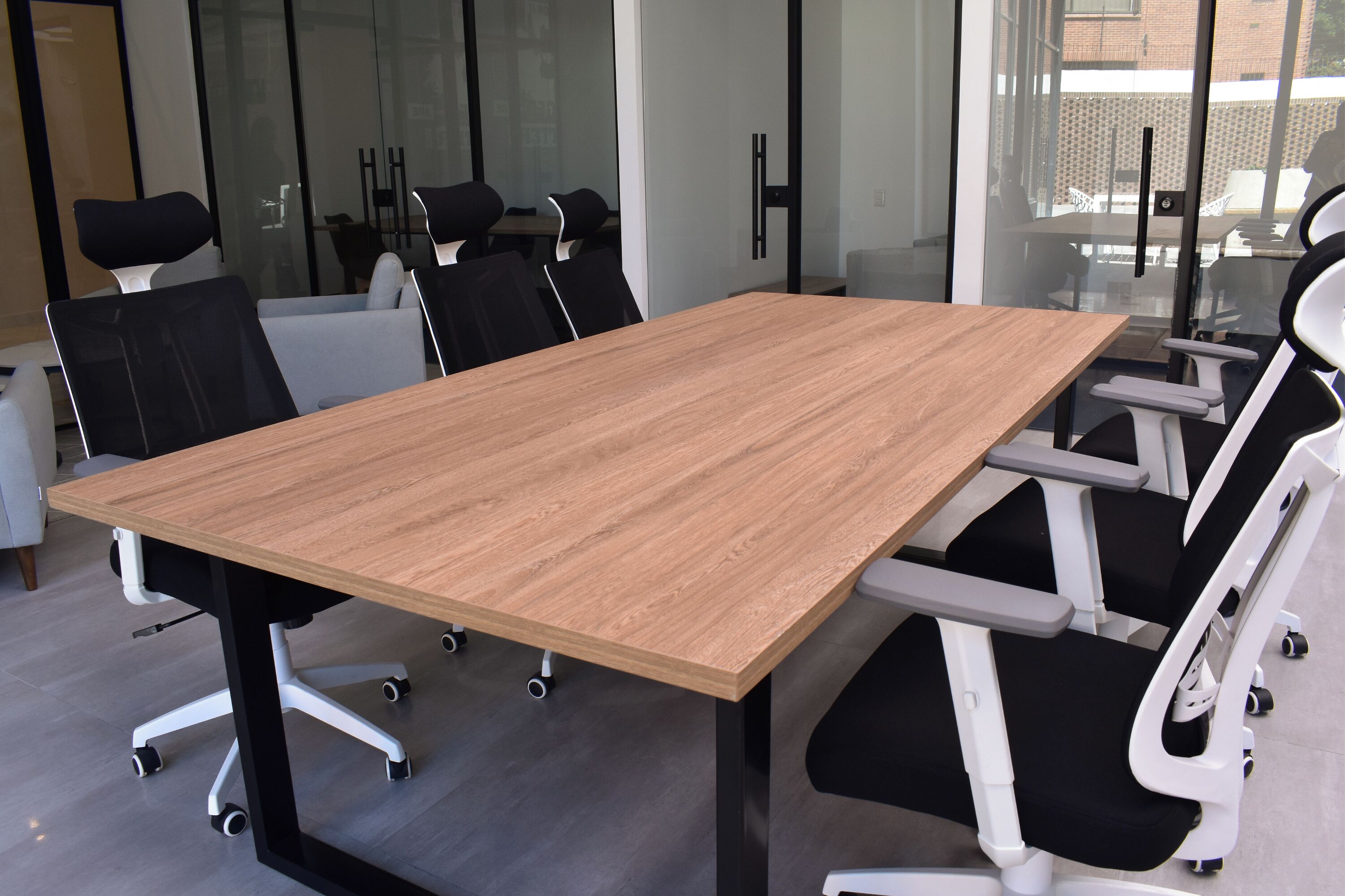 A conference room with a large wooden table, black and white chairs, and a glass partition.