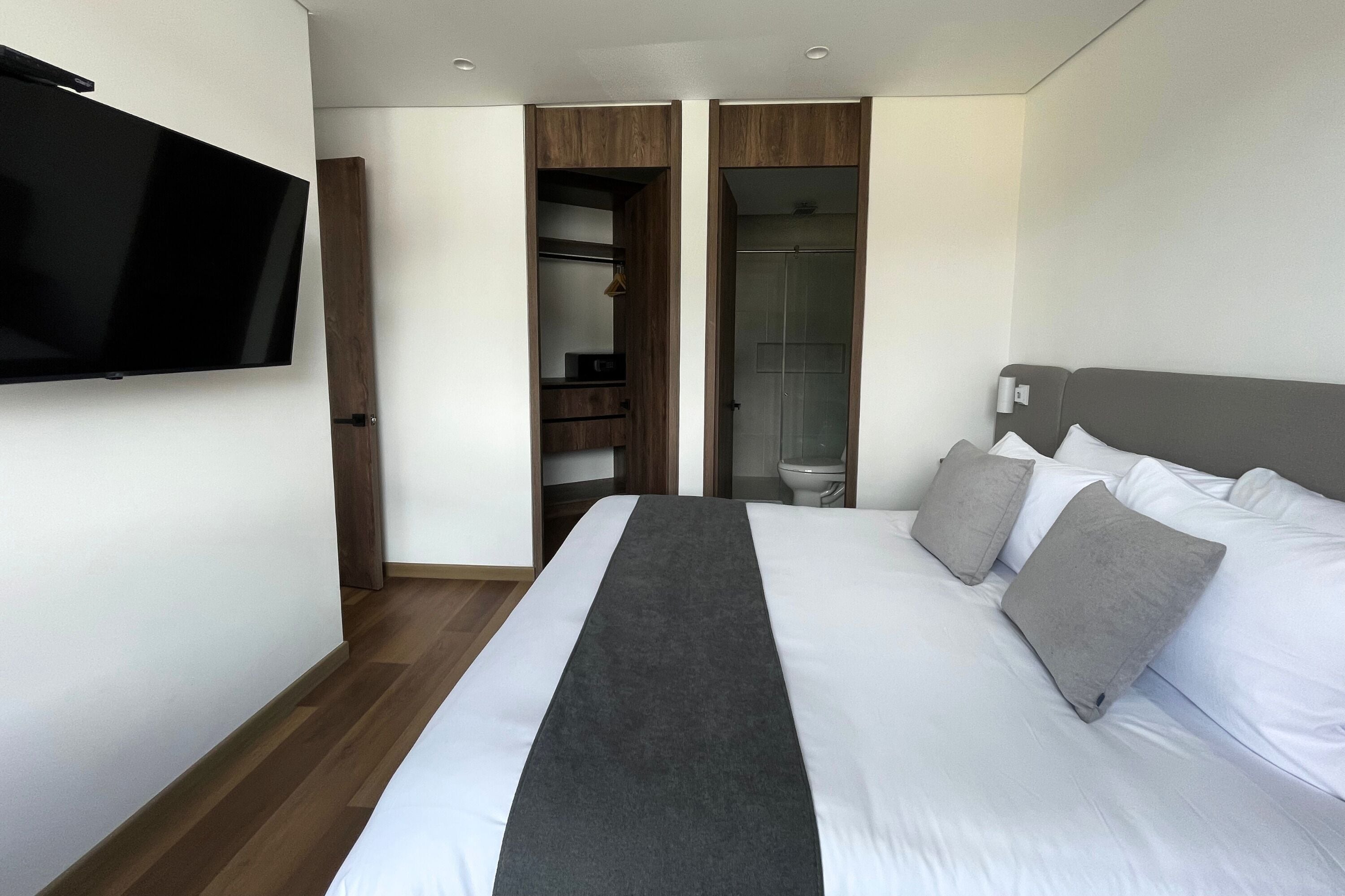 Een moderne hotelkamer met een groot bed, een flatscreen televisie aan de muur, een inloopkast en een zichtbare badkamer door een open deur.