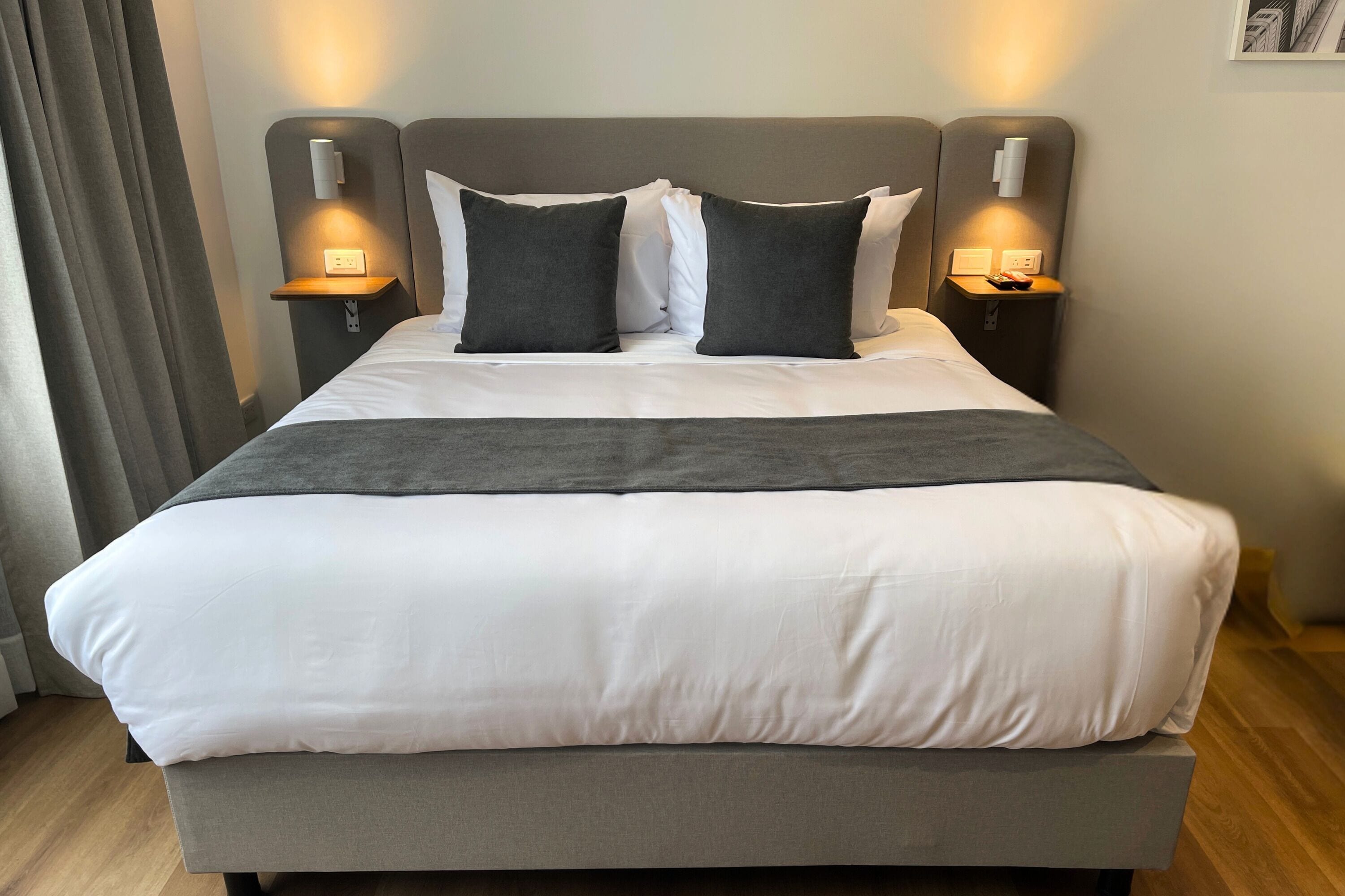 A neatly made bed with white and gray bedding, two bedside tables with lamps, and a wooden floor.