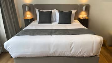 A neatly made bed with white and gray bedding, two bedside tables with lamps, and a wooden floor.