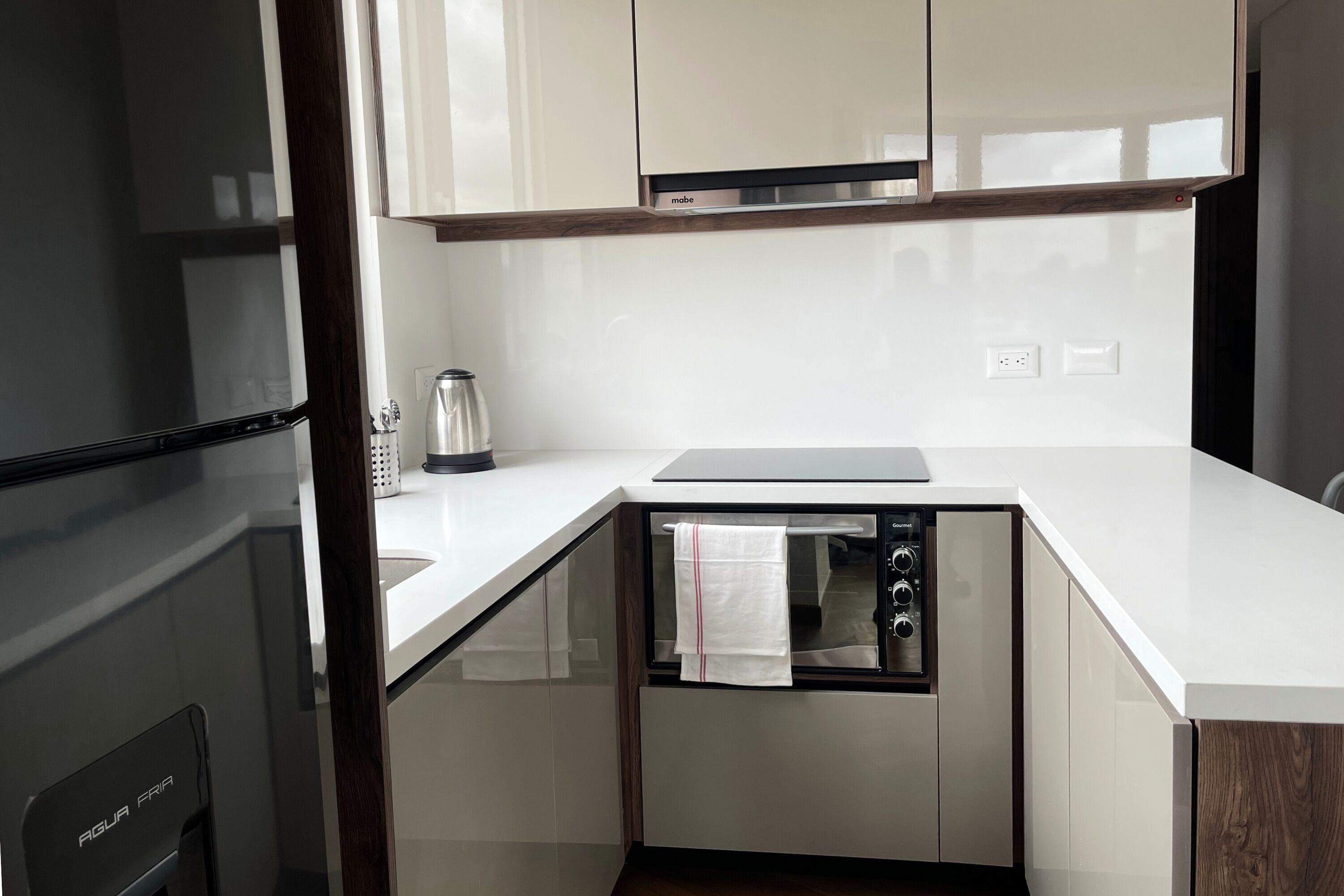 A modern kitchen with white cabinets, a built-in oven, and a stainless steel refrigerator.