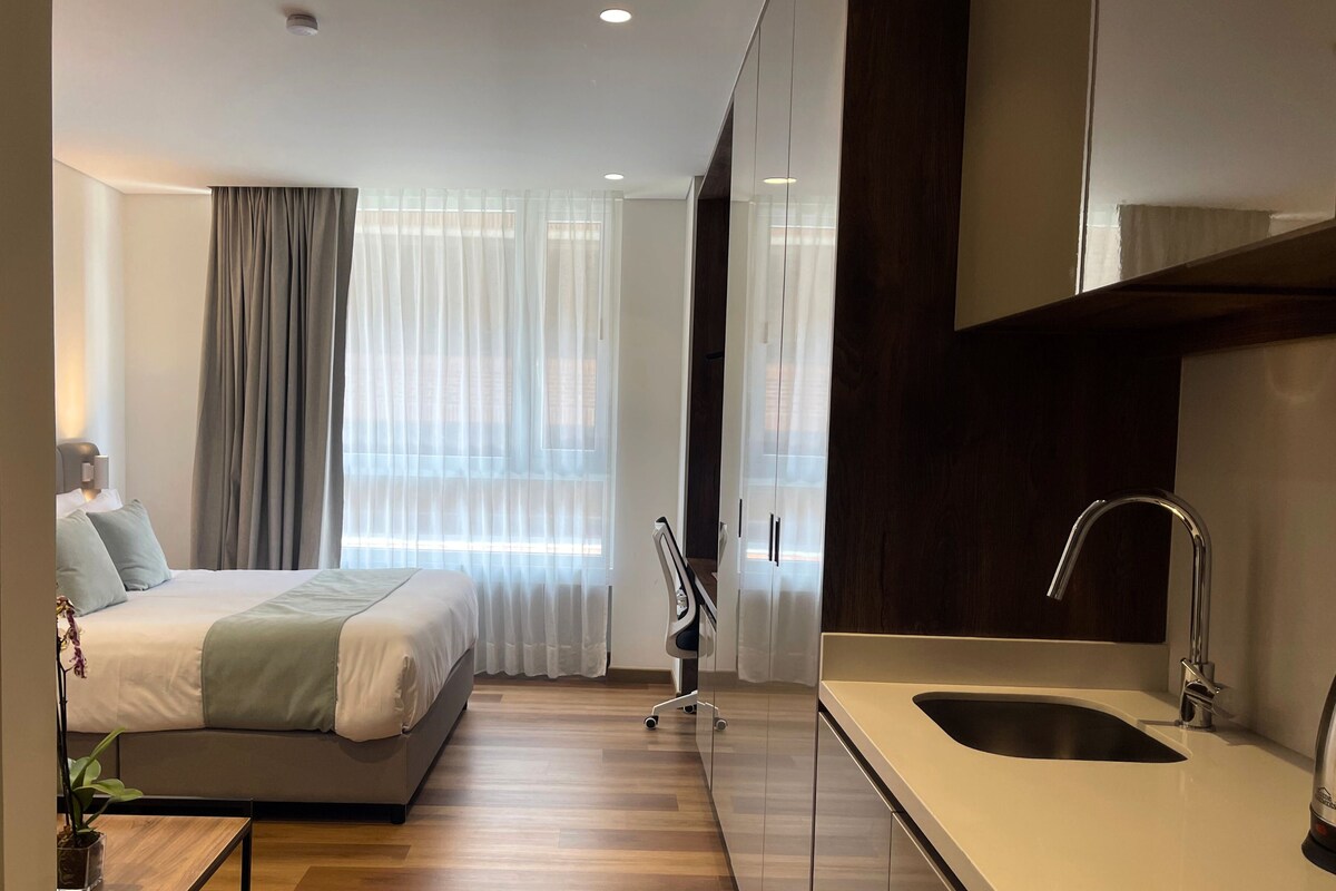 Een moderne hotelkamer met een groot bed, een bureau, een stoel, een wastafel en een raam met gordijnen.