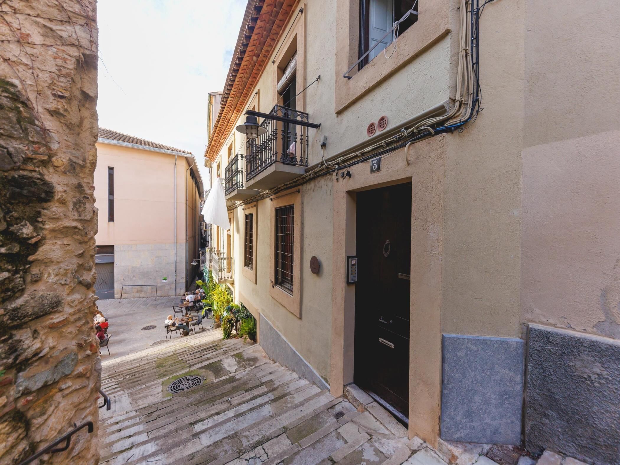Eine schmale Gasse mit Steinstufen, die zu einem Gebäude mit einer schwarzen Tür und einem Balkon führen.