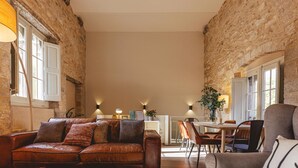Amplia sala de estar con sofá de cuero, un sofá gris y una mesa de comedor con sillas. La habitación cuenta con paredes de piedra vista y ventanas grandes.