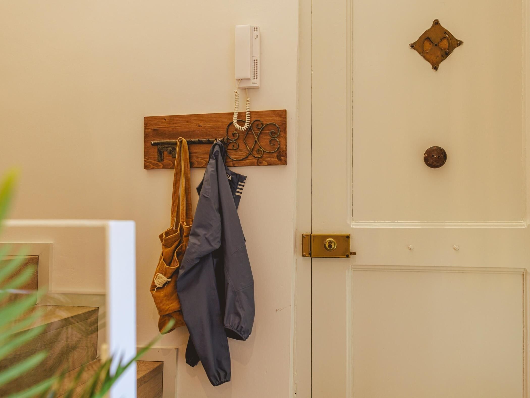 Een deur met een koperen deurklink, een houten plaquette met een symbool, en een aan de muur bevestigde telefoon.