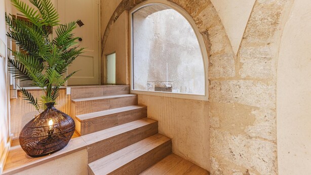 Una escalera con escalones de madera que conduce a una plataforma, un amplio ventanal de arco y una planta en maceta sobre la plataforma.