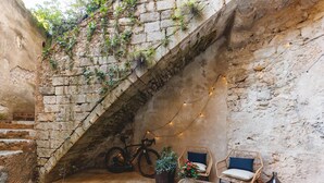 Un patio al aire libre con paredes de piedra, una bicicleta, muebles de mimbre e iluminación colgante.