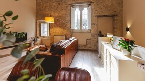 Una habitación acogedora con pared de piedra, un banco de madera, un armario blanco y una ventana con cortinas.