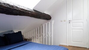 Un dormitorio con techo inclinado, una cama con colcha azul estampada, una puerta blanca y una barandilla blanca.