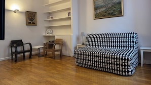 Una sala de estar con un sofá estampado, sillas de madera, una mesita, un ventilador y una estantería.