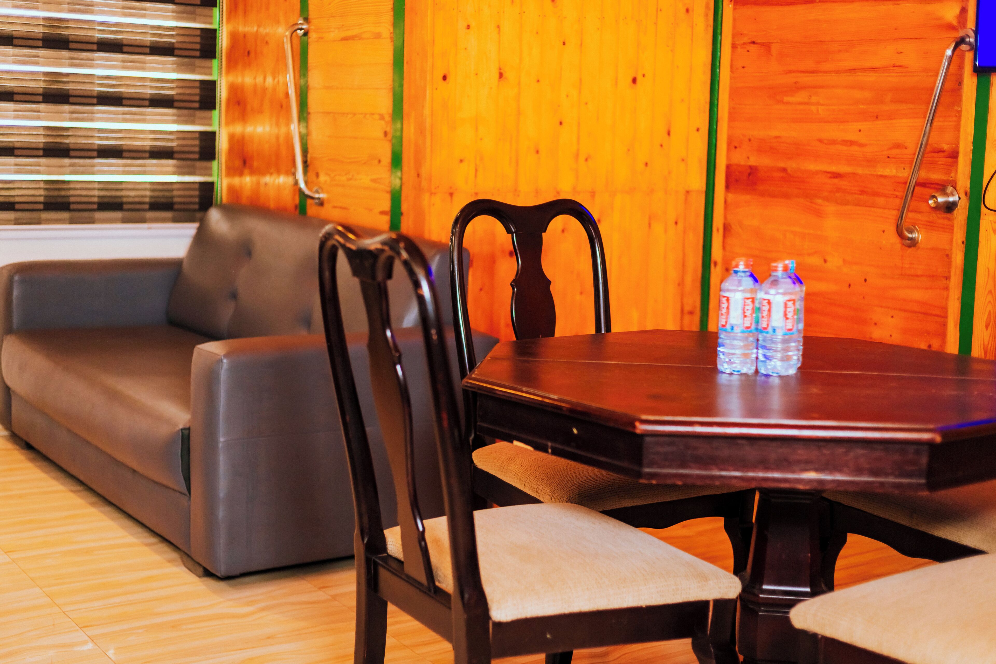 Un comedor con una mesa de madera, dos sillas, un sofá y dos botellas de agua sobre la mesa.