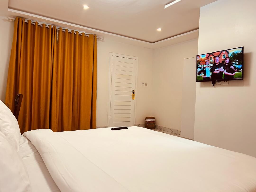 A hotel room with a bed, a television on the wall, and a door with a curtain.
