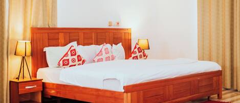 A wooden bed with white bedding and red patterned pillows, a bedside table with a lamp, and a red rug on a striped floor.