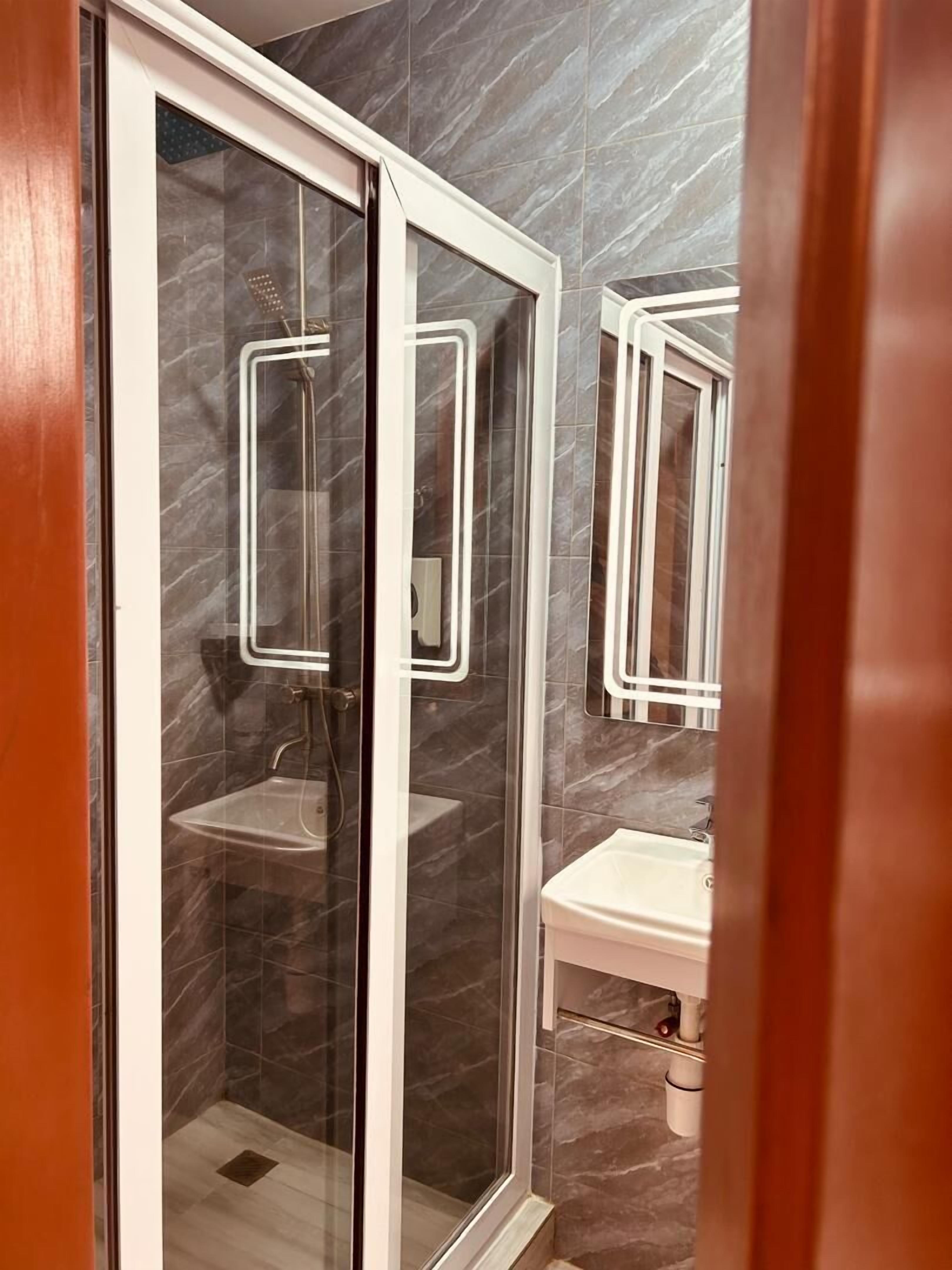 A modern bathroom with a glass-enclosed shower, a white sink, and a marble-tiled wall.
