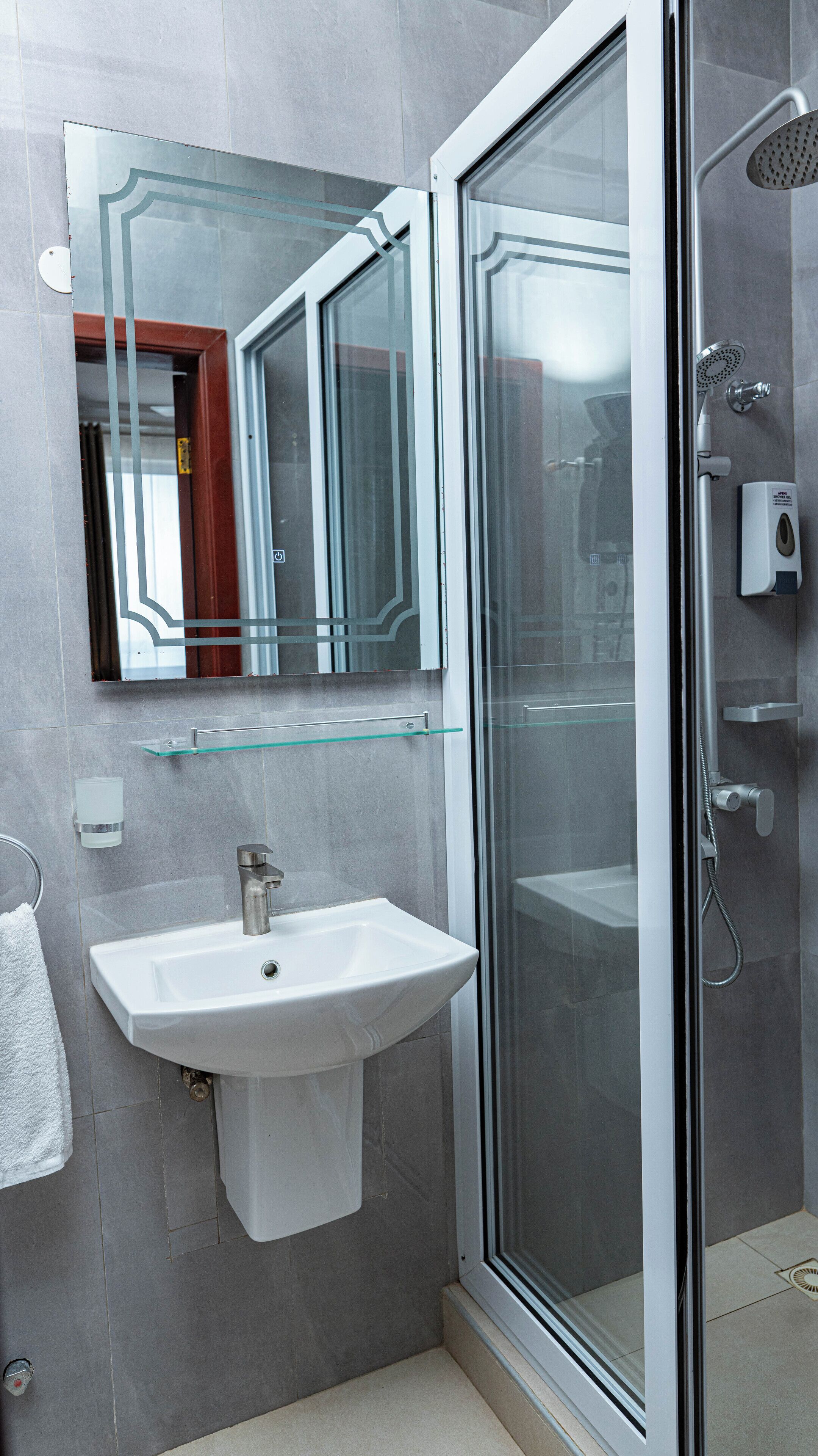 A modern bathroom with a glass shower enclosure, a white sink, and a glass shelf.