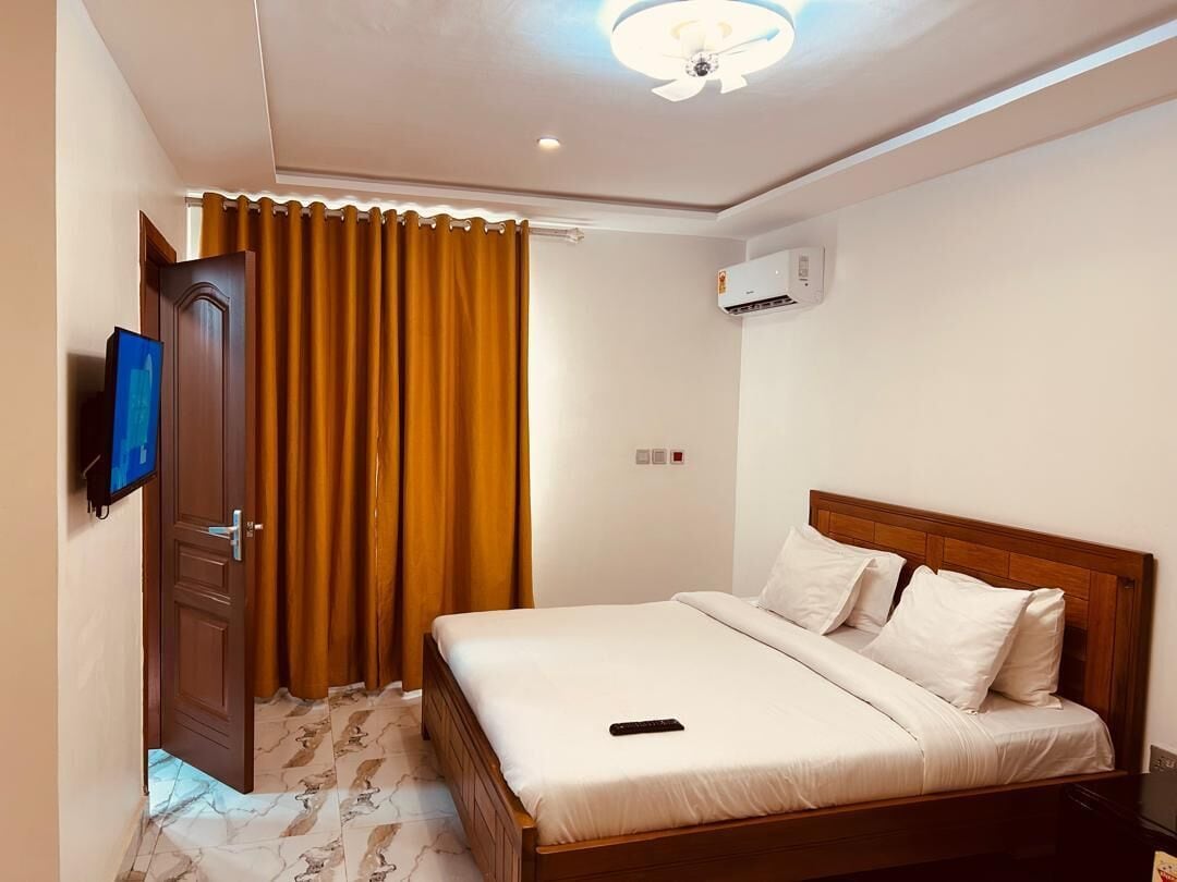 A hotel room with a bed, a television, a wardrobe, and an air conditioning unit.