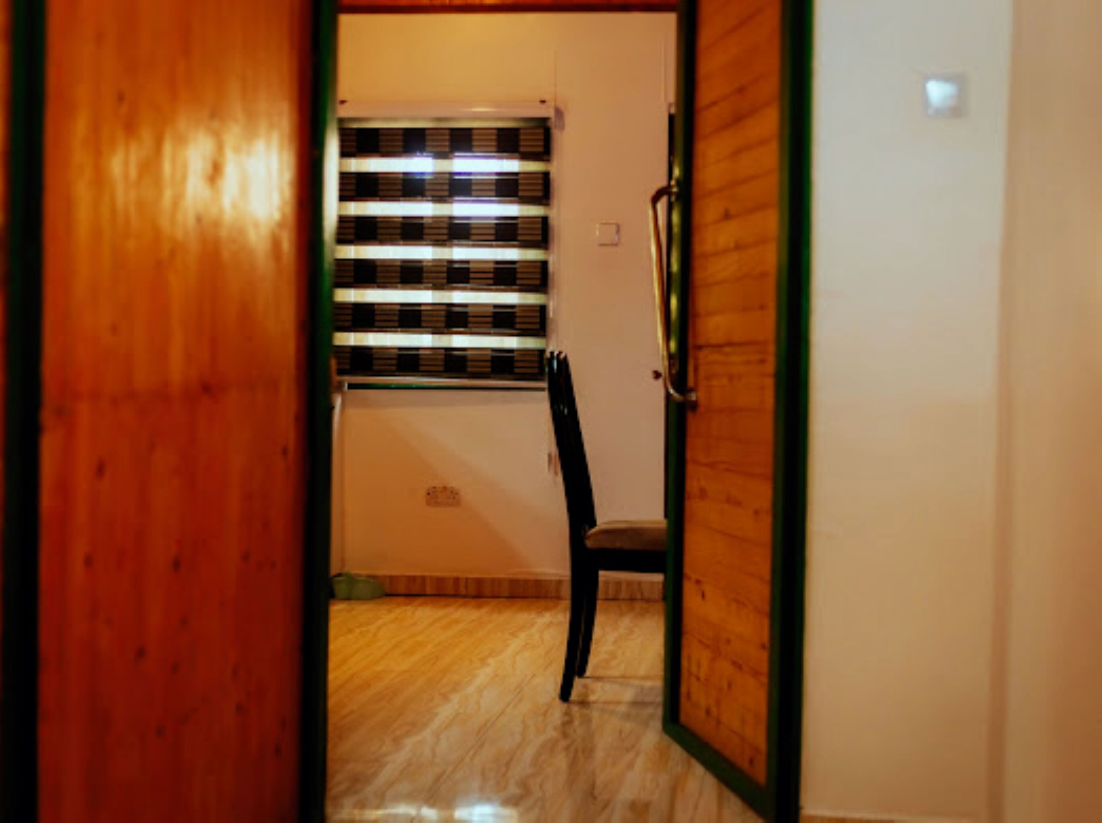 A hallway with a wooden door, a chair, and a window with blinds.