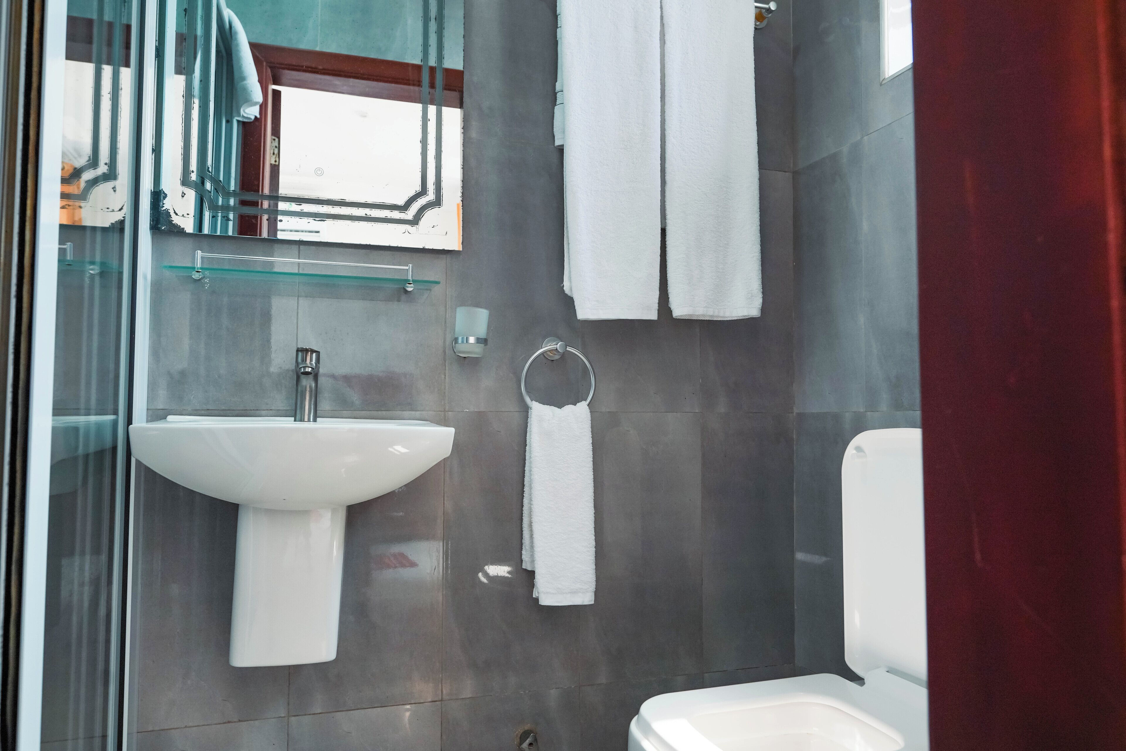 A modern bathroom with a glass shower enclosure, a pedestal sink, a toilet, and a towel rack.