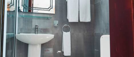 A modern bathroom with a glass shower enclosure, a pedestal sink, a toilet, and a towel rack.