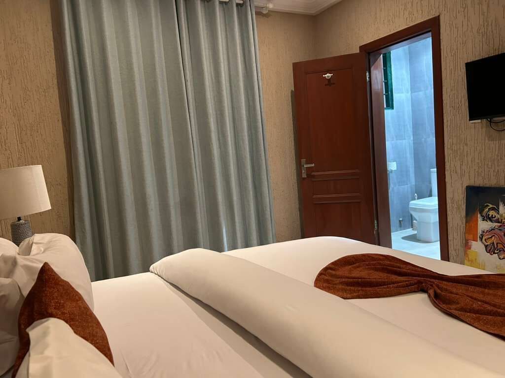 Habitación de hotel con cama, mesita de noche con lámpara, puerta al baño y televisor montado en la pared.