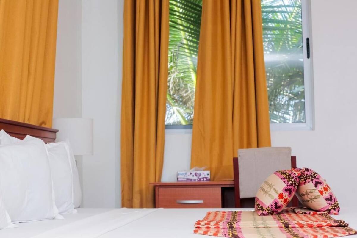 Quarto de hotel com cama, mesa de cabeceira, cadeira e janela com cortinas.
