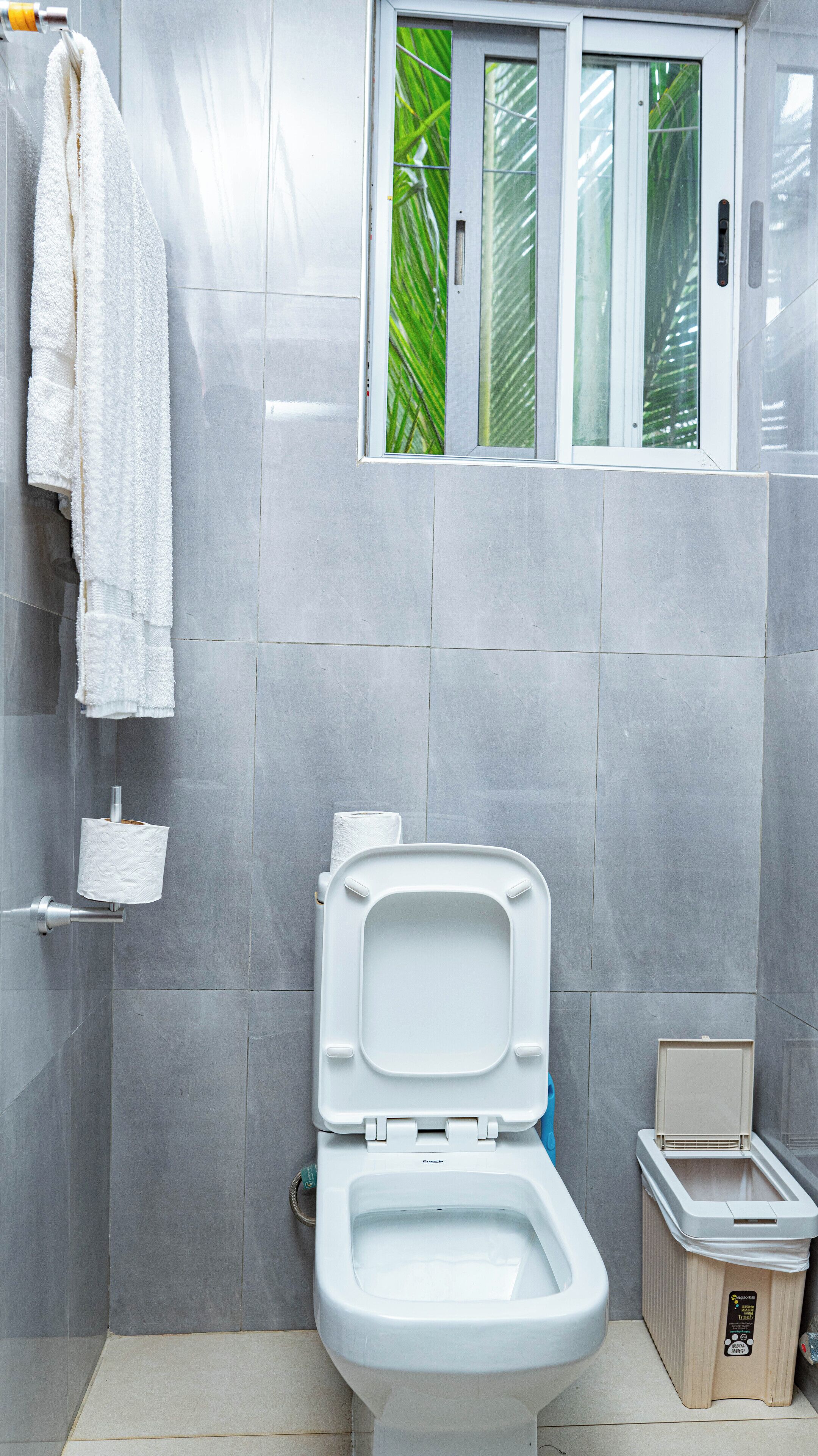 A bathroom with a toilet, a towel rack, and a window with a view of greenery.