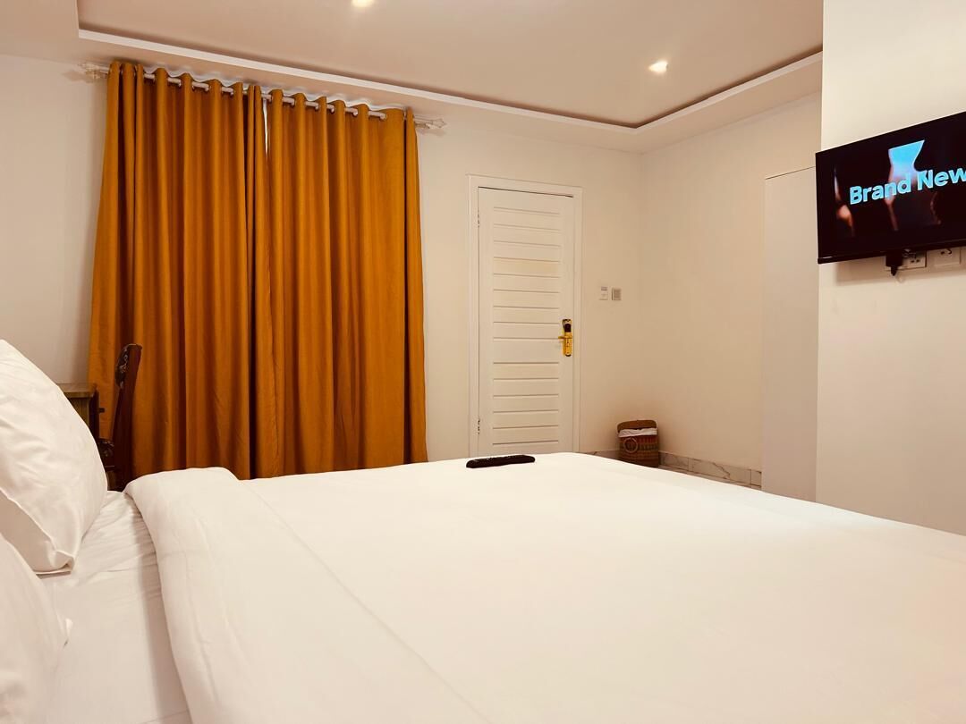 Habitación de hotel con cama, televisor montado en la pared y puerta con manija.
