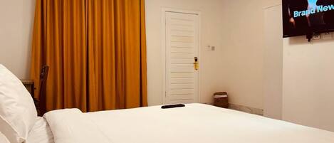 Habitación de hotel con cama, televisor montado en la pared y puerta con manija.