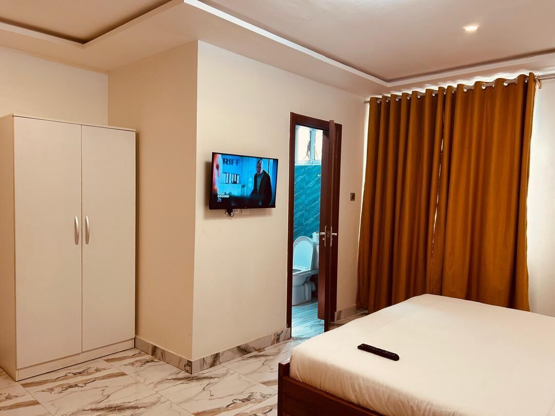 A hotel room with a bed, a TV mounted on the wall, a wardrobe, and a bathroom visible through an open door.