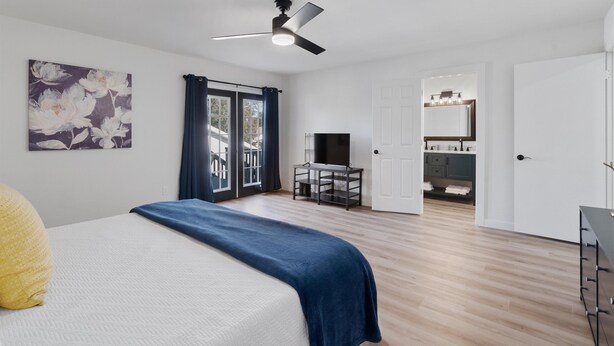 A bedroom with a bed, a ceiling fan, a TV, and a bathroom visible through an open door.