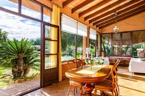 Un comedor con mesa y sillas de madera, una ventana con cortinas y vista a follaje exterior.