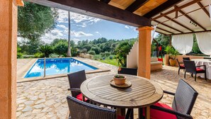Un espacio al aire libre cubierto con piscina, suelo de piedra, mobiliario de mimbre y una mesa con planta en maceta.