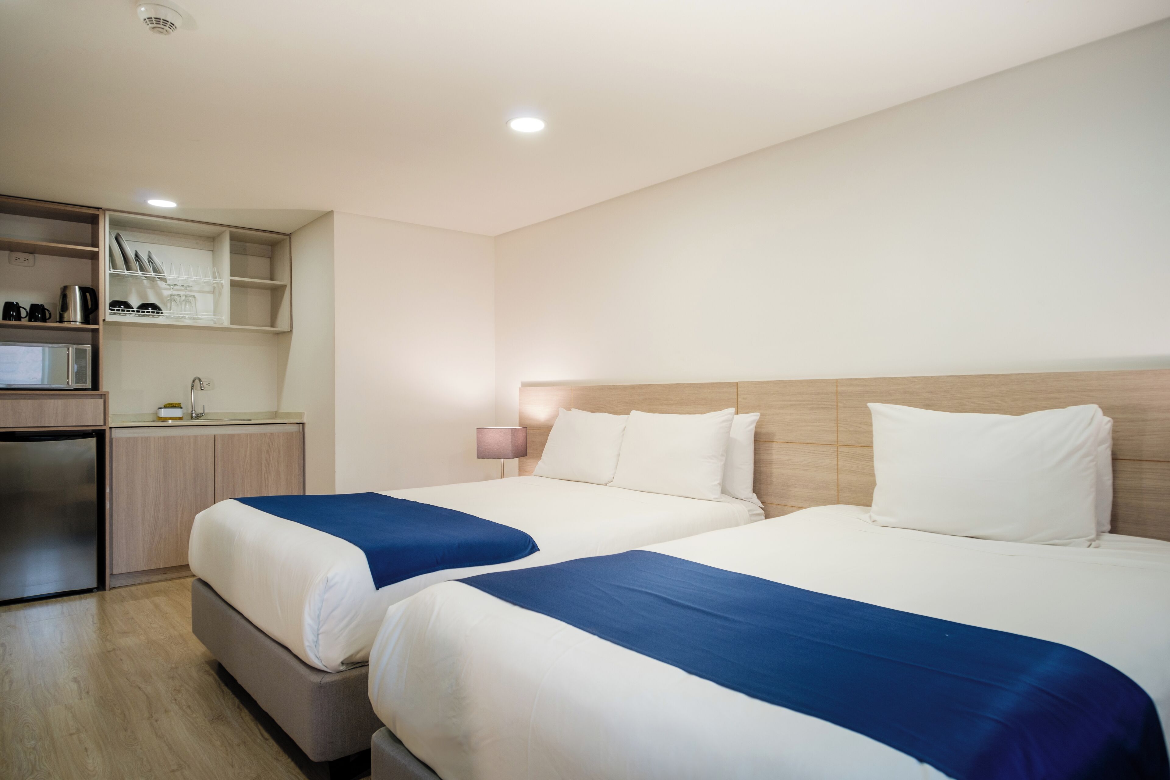 Hotellihuone, jossa on kaksi sänkyä, pieni keittiönurkkaus ja pieni työpöytä.