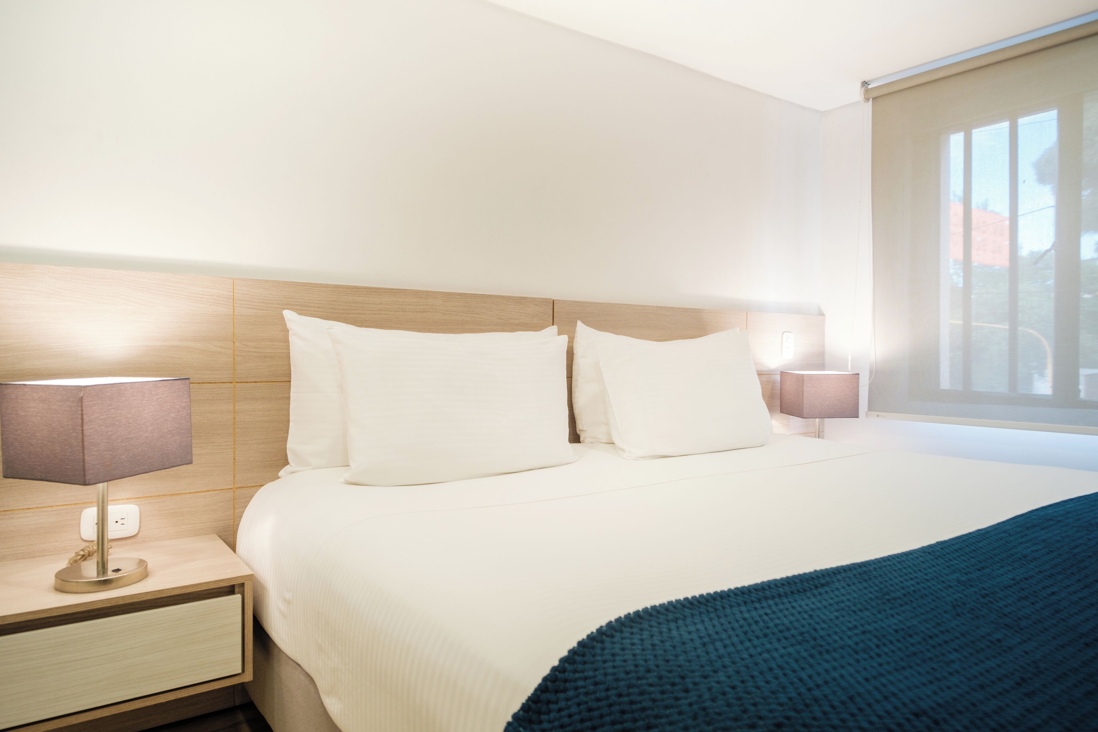 Una habitación de hotel con una cama grande, dos mesitas de noche con lámparas y un alfeizar con cortinas.