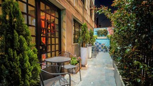 Une terrasse extérieure avec une table et des chaises, entourée de verdure et dotée d’un sol carrelé.