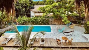 A pool area with a thatched roof, lounge chairs, and a hammock. - Kawabonga Hostel (Dibulla)