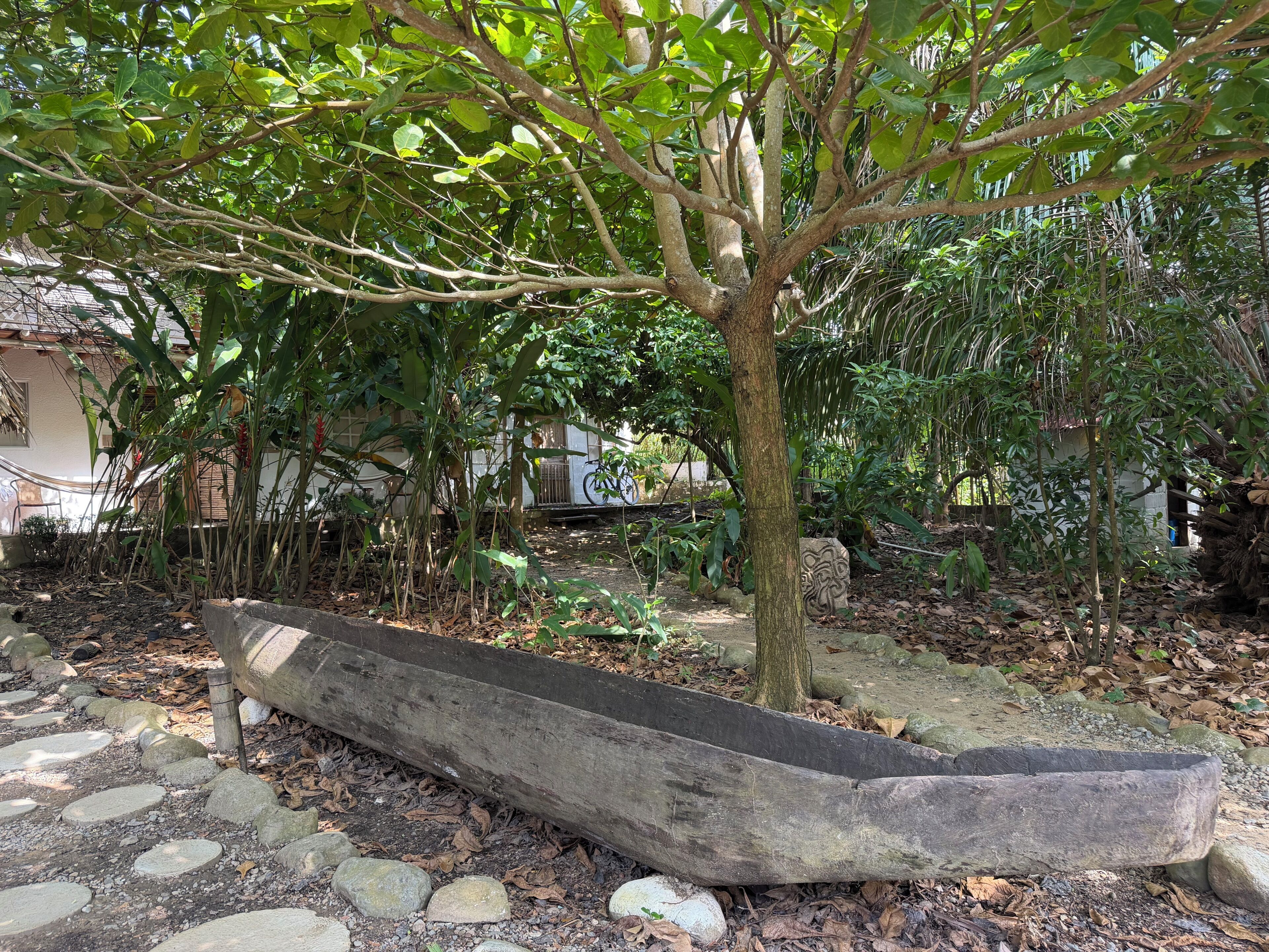 A garden with a large tree, a stone pathway, and a wooden boat.