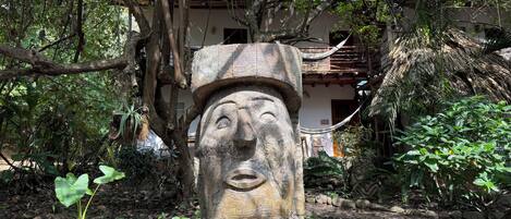 A stone statue in a garden with trees and a building in the background.