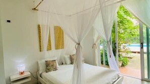 A bedroom with a canopy bed, a bedside table with a lamp, and a view of greenery outside. - Kawabonga Hostel (Dibulla)