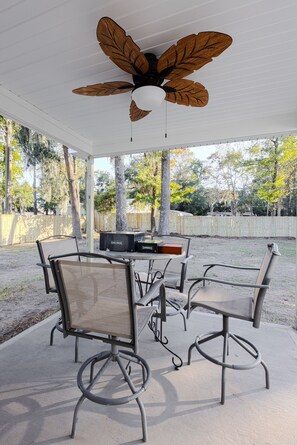 Un patio couvert avec un ventilateur de plafond, des sièges d’extérieur et un barbecue.