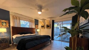 Une chambre à coucher avec un lit, un ventilateur de plafond, une table de chevet et une grande fenêtre.
