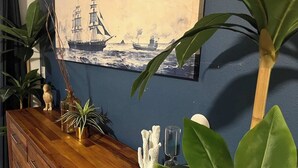 Une commode en bois agrémentée d’objets décoratifs et un tableau maritime encadré, le tout sur un mur bleu.
