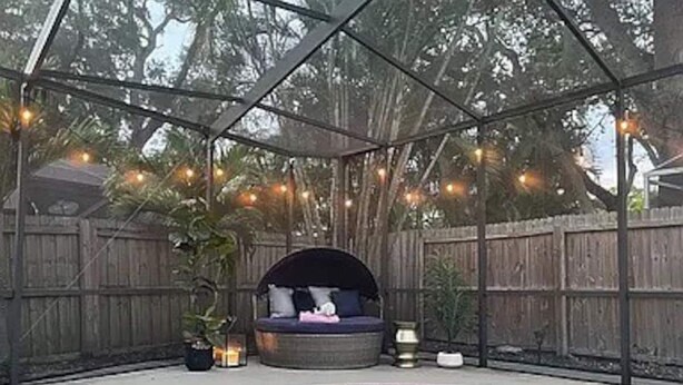Une piscine dotée d’un jacuzzi et d’un espace détente, le tout entouré d’une clôture en bois et illuminé de guirlandes lumineuses.
