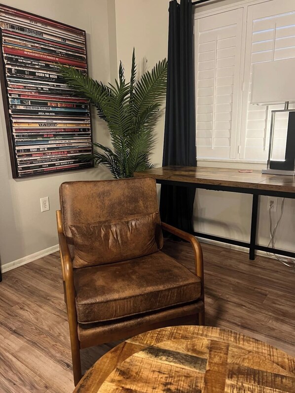 A living room with a brown leather chair, a coffee table, a plant, a wall-mounted CD rack, and a window with curtains. - Your pet friendly Tampa pool home, right between the beaches and Tampa proper! (Largo)