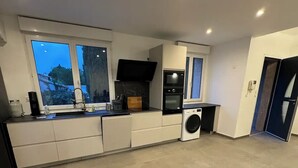 A modern kitchen with a built-in oven, microwave, and washing machine. There are large windows providing natural light and a view of the outside. - Family villa with pool, air-conditioning & independent studio. (Valergues)