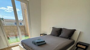 A bedroom with a large bed, a small bedside table, and a view of a green outdoor area through a sliding glass door. - Family villa with pool, air-conditioning & independent studio. (Valergues)